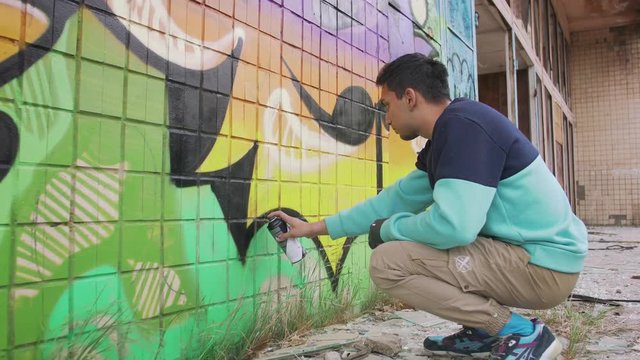 Young man graffiti artist painting on the wall, exterior