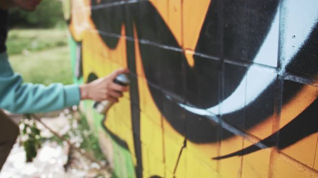 Young man graffiti artist painting on the wall, close up, slow motion