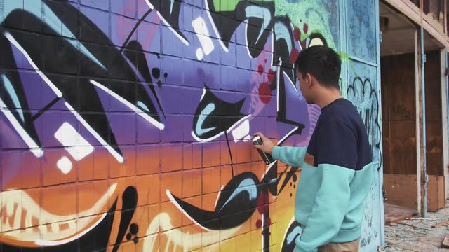 Young man graffiti artist painting on the wall, exterior