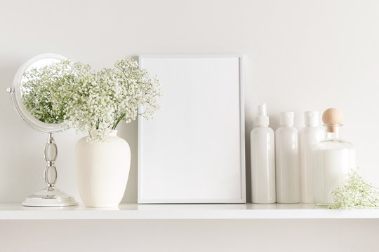 Cosmetic set on light dressing table.Beautiful flowers in a vase on a white wall background, mirror on a wooden shelf.