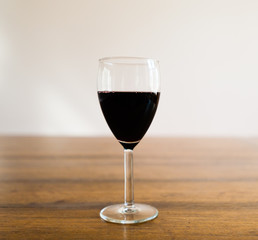 Glass of red wine on wood table against white wall.