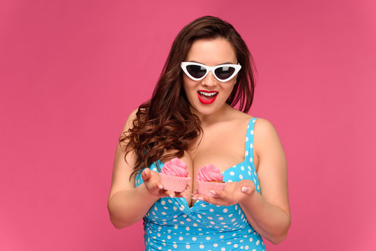 beautiful smiling woman in swimsuit and sunglasses holding delicious cupcakes isolated on pink
