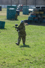 Paintball player in camouflage uniform and protective mask with gun on the field, shoot into enemies in the summer 