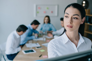 Fototapeta premium selective focus of pensive businesswoman and colleagues behind at workplace in office