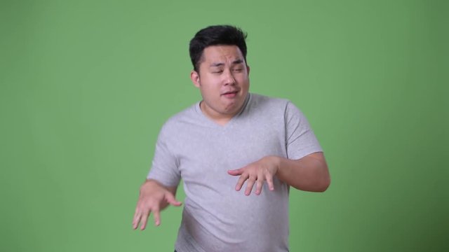 Young handsome overweight Asian man against green background