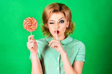 Lollipop. Sweet food, dessert, sugar. Pin up model with lollipop in hand. Sexy funny retro fashion girl in summer dress with colourful candy. Copy space for advertising. Isolated on green background.