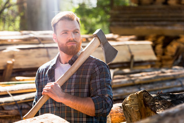 lumberjack in checkered shirt holding axe on shoulder at sawmill