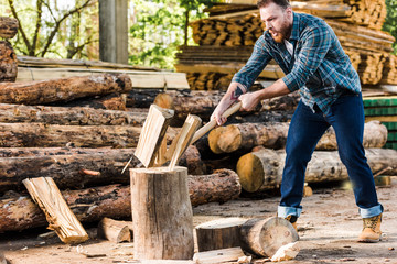  lumberjack in checkered shirt chopping log at sawmill
