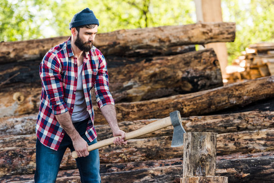 bearded lumberjack in checkered shirt chopping log at sawmill