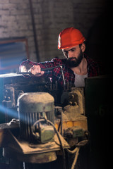 worker in protective helmet repairing machine tool at sawmill