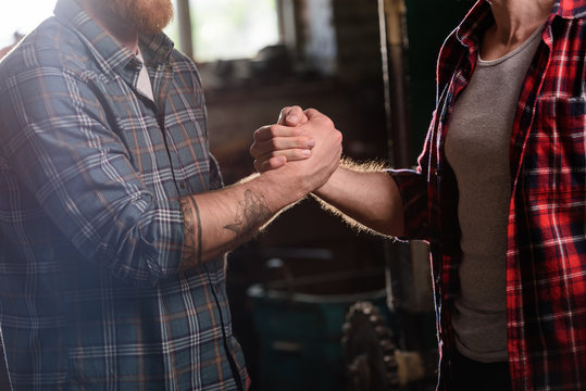 cropped image of carpenter with tattooed hand shaking hand of partner at sawmill