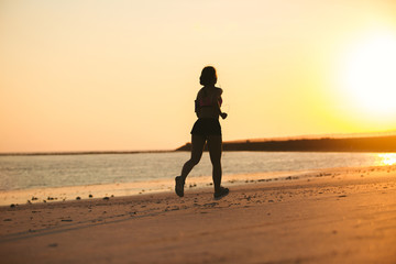 rear view of silhouette of sportswoman running on beach against sunlight