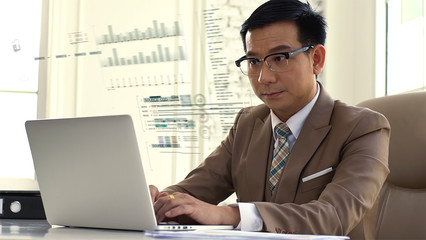 An Asian businessman Working on a laptop looking intense and seriousness about the company’s sales figures performance