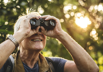 Mature man watching birds through binoculars - obrazy, fototapety, plakaty