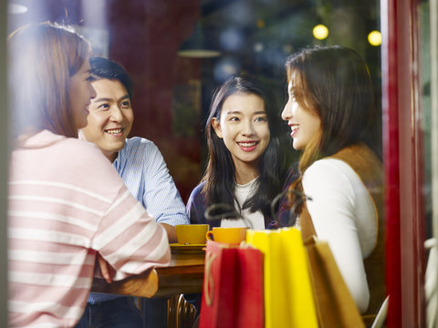 four young asian adults chatting talking in coffee shop after shopping