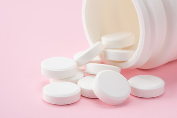 closed up white round pill pouring out of the bottle on pink background