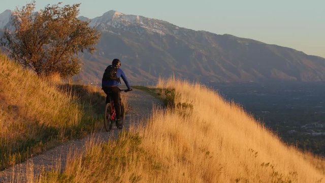 A mountain biker rides a trail in the Wasatch Mountains, overlooking Salt Lake City at sunset.