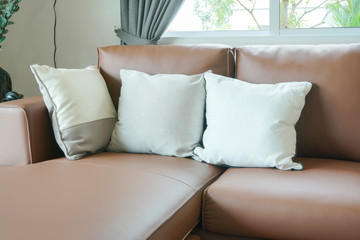 Light brown leather sofa with pillows next to window in the living room