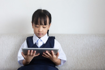 Asian Chinese little girl sitting on the sofa playing digital tablet