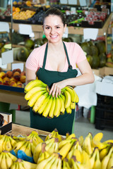 smiling attractive salesgirl proposing fresh bananas in supermarket