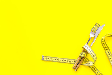 Diet, weight loss, slimming concept. Fork and knife with wound measuring tape on yellow background...