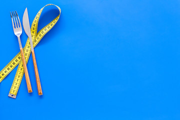 Diet, weight loss, slimming concept. Fork and knife with wound measuring tape on blue background...