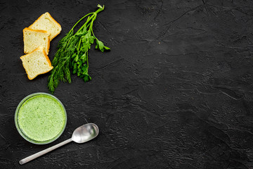 Natural, organic food. Green vegetable soup-puree in bowl ready to eat served with rusks on black table top view copy space