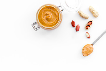 Peanut butter in glass jar near peanut on white background top view copy space