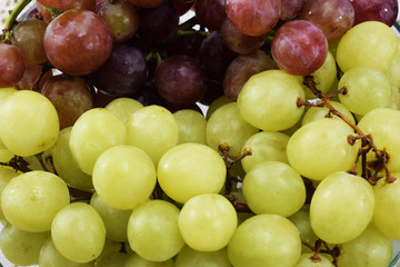 Brushes of fresh grapes of different kinds on a beautiful saucer on a wooden table
