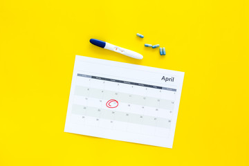 Planning pregnancy. Positive pregnancy test near calendar page and pills on yellow background top view copy space