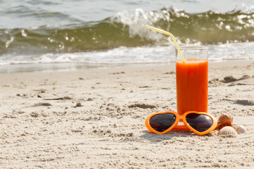Carrot juice and sunglasses at beach, concept of vitamin A and beautiful, lasting tan