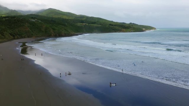 Wide drone shot of a cloudy New Zealand beach with surfers and horse riders