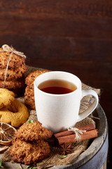 Conceptual festive composition with a cup of hot tea, cookies and spicies on a wooden barrel, selective focus, close-up