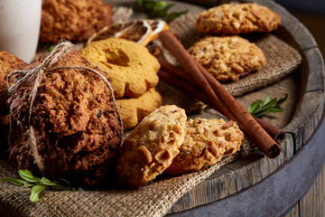Conceptual composition with assortment of cookies and cinnamon with napkin on a wooden barrel, selective focus