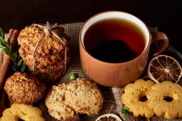 Festive composition with a mug of hot tea, cookies and spicies on a wooden barrel, selective focus, close-up
