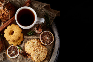 Conceptual festive composition with a cup of hot tea, cookies and spicies on a wooden barrel, selective focus, close-up