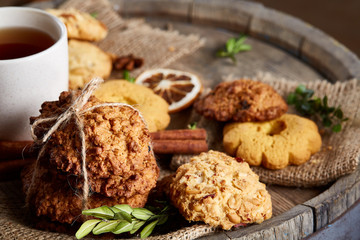 Conceptual festive composition with a cup of hot tea, cookies and spicies on a wooden barrel, selective focus, close-up