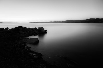 Dusk on a lake, with rocks in the foreground, perfectly still wa