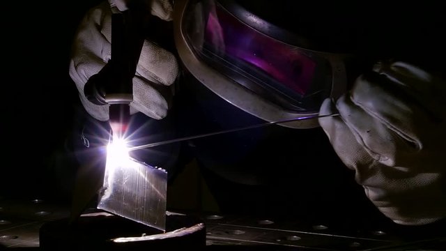 A professional worker holds a welding machine in his hands to form a welded seam