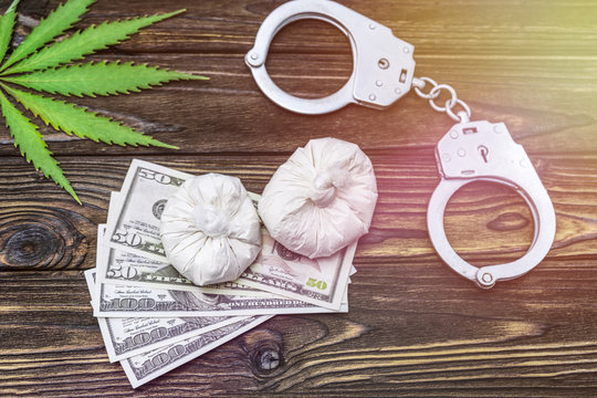 drugs, hemp. dollars, iron handcuffs on the background of a wooden table. law violation