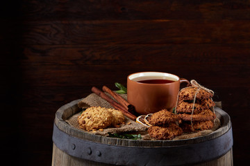 Conceptual festive composition with a cup of hot tea, cookies and spicies on a wooden barrel, selective focus, close-up