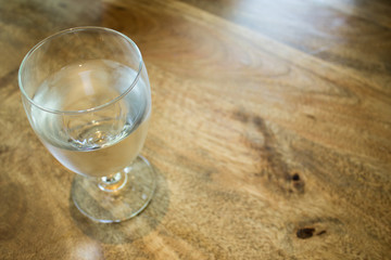Glass of water on wooden table with reflection and wood grain.  Glass half full or glass half empty.