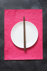 Asian style tableware. White plate with bamboo chopsticks on red napkin. Top view.