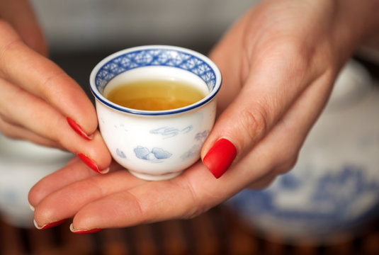 Cropped shot of woman holding traditional chinense teacup with oolong green tea.