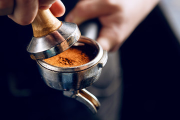 Barista holding portafilter and coffee tamper making an espresso coffee.