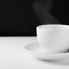 White mug for tea with a hot drink on a white wooden table on a black background. Close up