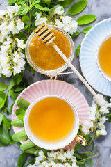Vintage cups with tea next to a jar of honey and acacia on a gray table. Tea with natural sweetener honey. Top view, flat lay