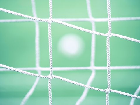 View through football gate net. Soccer ball on green grass