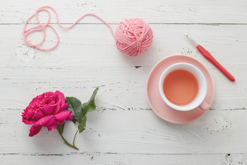 Cup of tea with pink ball of yarn, crochet hook and rose on white background.