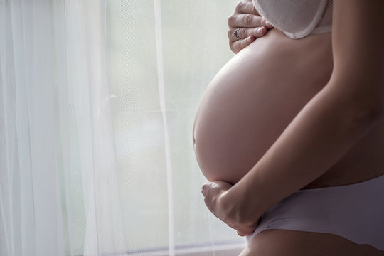 belly of a pregnant woman beside the window with curtains